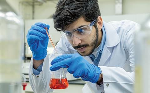A scientist looking at red liquid in a vial